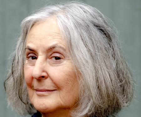 Smiling older person with shoulder-length gray hair, wearing a black top and blue cardigan