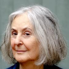 Smiling older person with shoulder-length gray hair, wearing a black top and blue cardigan