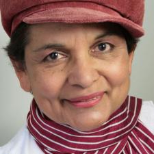 Lakshmi Persaud wearing a pinky red cap and scrarf, smiling