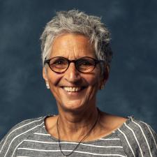 Seni Seneviratne smiling, wearing a grey striped top and glasses
