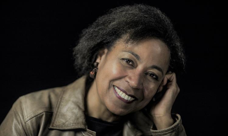 Alecia McKenzie, a black woman smiling, leaning her face into hand
