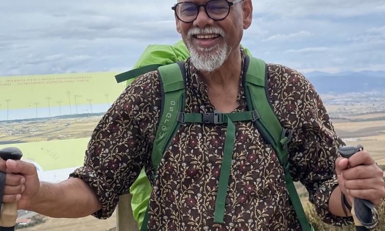 Manzu Islam hiking with white beard and glassesrucksack and poles, smiling